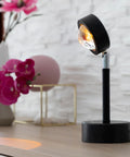 Lampada proiettore tramonto su tavolo con fiori rosa in ambiente moderno, illuminazione speciale per decorazione e atmosfera accogliente